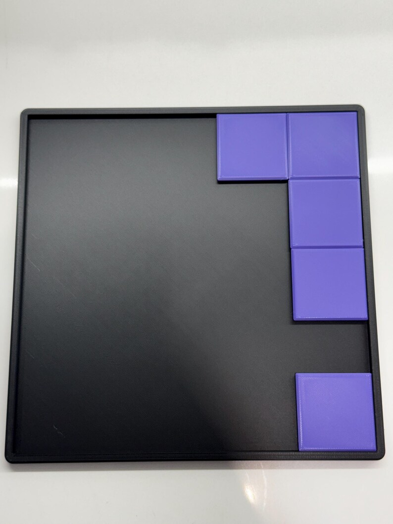 Pu&ograve; includere: Un vassoio nero con un puzzle di piastrelle viola. Il puzzle &egrave; composto da cinque piastrelle quadrate disposte a forma di L.