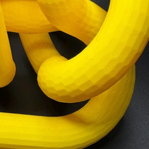 May include: A yellow 3D printed sculpture with a smooth, textured surface. The sculpture is made up of multiple interlocking loops.