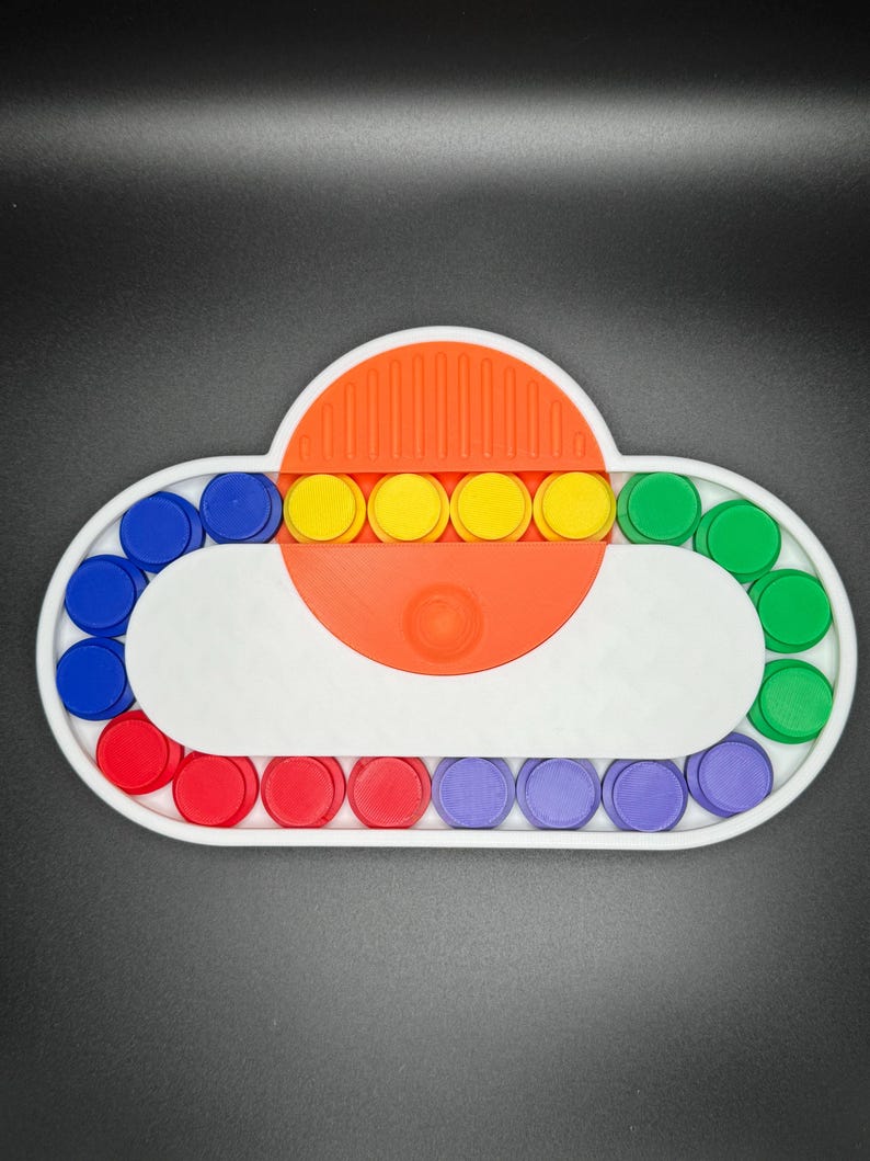 May include: A white cloud-shaped sensory toy with a red, blue, green, and yellow circle pattern. The toy has a central orange section with a series of yellow circles.