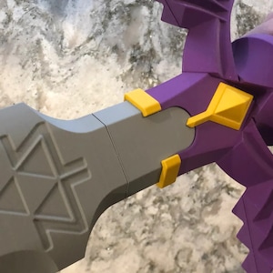 May include: A purple and yellow plastic sword with a triangular design on the blade. The sword is held by a hand.