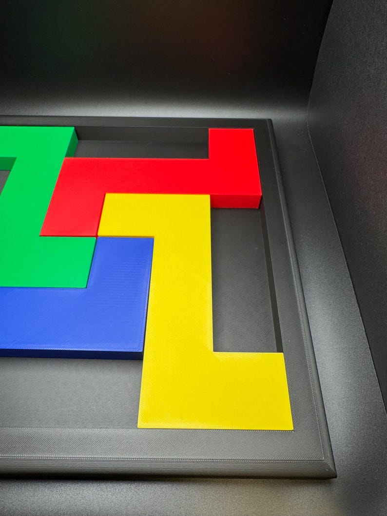 Op de afbeelding: Een kleurrijke puzzel met vier L-vormige stukken in groen, rood, blauw en geel, gerangschikt in een donkergrijs frame. De stukken zijn in elkaar verweven en cre&euml;ren een geometrisch ontwerp. Het frame heeft een getextureerd oppervlak.