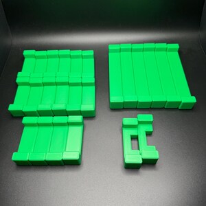 May include: A set of four green plastic building blocks. The blocks are rectangular and have a smooth surface. They are arranged in a pattern on a black surface.