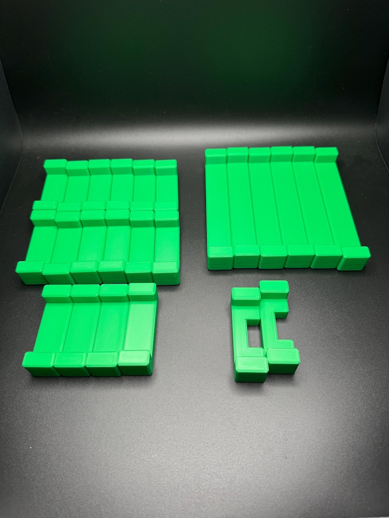 May include: A set of four green plastic building blocks. The blocks are rectangular and have a smooth surface. They are arranged in a pattern on a black surface.