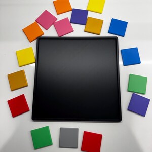 Pu&ograve; includere: Un tabellone quadrato nero circondato da piastrelle quadrate colorate in varie tonalit&agrave; di rosso, arancione, giallo, verde, blu, viola e rosa.