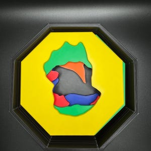 Op de afbeelding: Een geel achtkantig frame met een veelkleurig abstract ontwerp erin. Het ontwerp is gemaakt van groene, oranje, rode, blauwe en zwarte vormen.