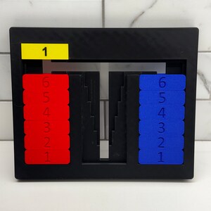 May include: A black frame with a yellow label that says "1" and two sets of red and blue number tiles. The red tiles are numbered 1 through 6 and the blue tiles are numbered 1 through 6.