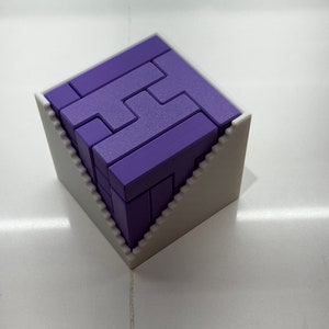 Puede incluir: Un rompecabezas 3D de color morado en forma de cubo, ensamblado dentro de un marco blanco con un dise&ntilde;o escalonado.
