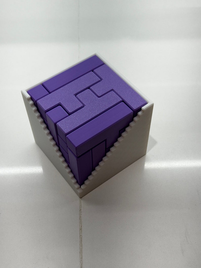 Puede incluir: Un rompecabezas 3D de color morado en forma de cubo, ensamblado dentro de un marco blanco con un dise&ntilde;o escalonado.
