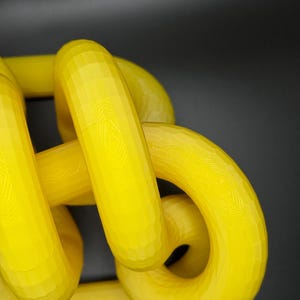 May include: A yellow 3D printed sculpture of a knot. The knot is made of multiple loops that are intertwined with each other.