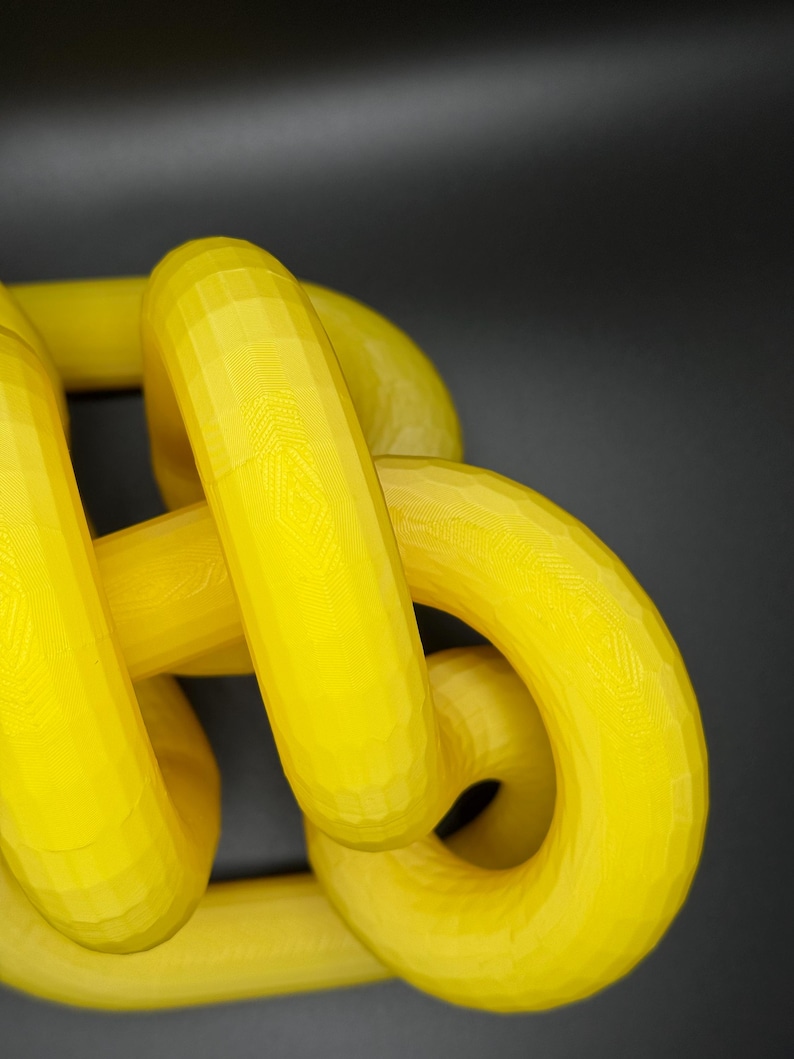 May include: A yellow 3D printed sculpture of a knot. The knot is made of multiple loops that are intertwined with each other.