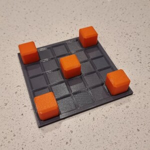 May include: A gray game board with a grid pattern and five orange cubes on top. The cubes are arranged in a cross shape.