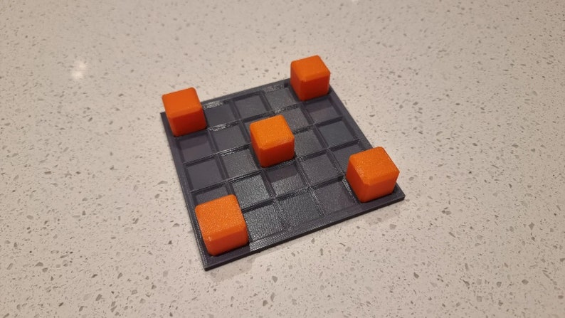 May include: A gray game board with a grid pattern and five orange cubes on top. The cubes are arranged in a cross shape.