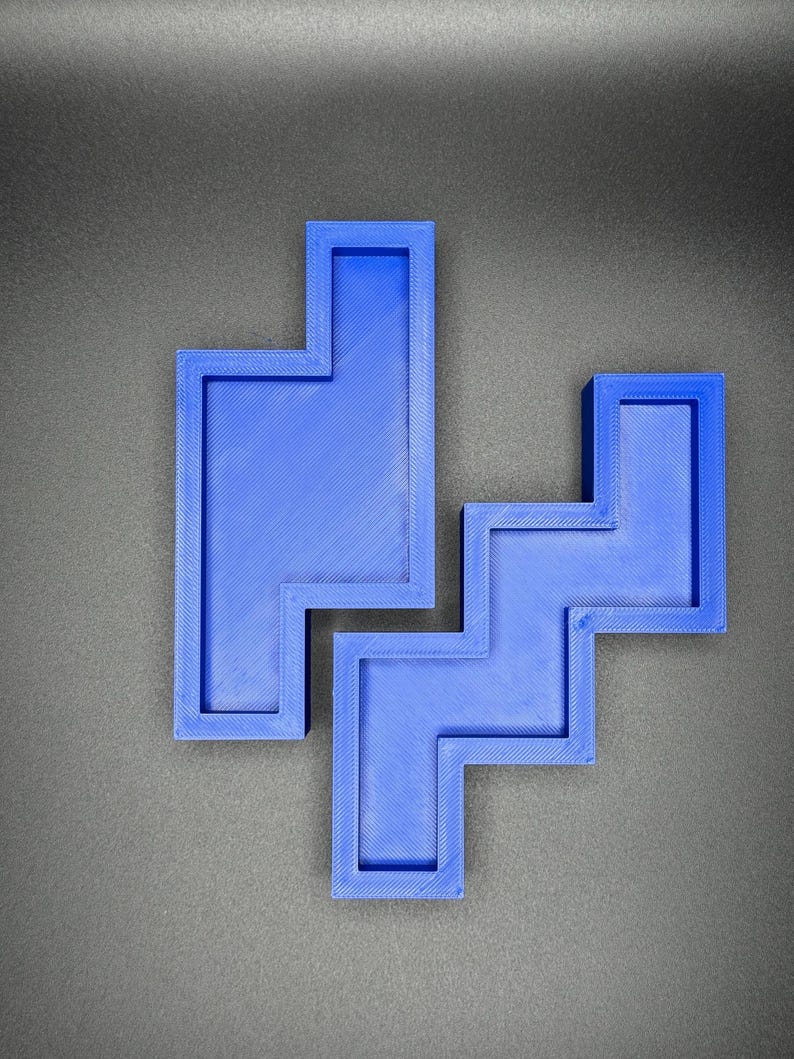 May include: A blue plastic puzzle with a unique shape, resembling a combination of squares and rectangles. The puzzle is made up of two separate pieces that fit together.