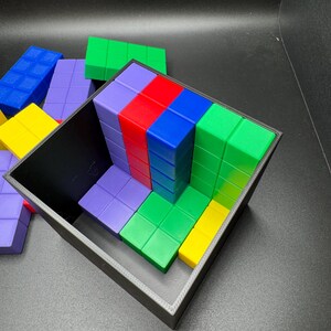May include: A black container filled with colorful, rectangular blocks. The blocks are arranged in rows and columns, with colors including red, blue, green, yellow, and purple. Some blocks are outside the container.
