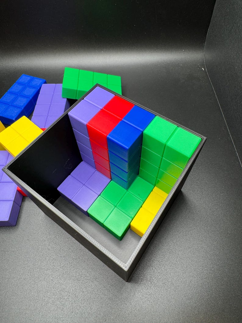 May include: A black container filled with colorful, rectangular blocks. The blocks are arranged in rows and columns, with colors including red, blue, green, yellow, and purple. Some blocks are outside the container.