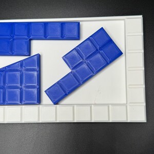 May include: Blue plastic puzzle pieces on a white puzzle board. The pieces are shaped like rectangles and squares.