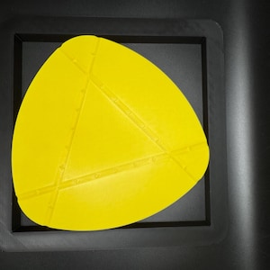 K&ouml;nnte beinhalten: Eine gelbe, dreieckige Silikonform mit strukturierter Oberfl&auml;che. Die Form befindet sich in einem schwarzen Rahmen.