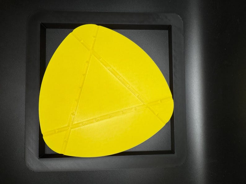 K&ouml;nnte beinhalten: Eine gelbe, dreieckige Silikonform mit strukturierter Oberfl&auml;che. Die Form befindet sich in einem schwarzen Rahmen.
