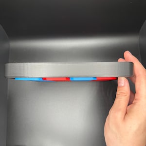 Pu&ograve; includere: Un vassoio di plastica nero con un bordo rialzato, che contiene un set di piastrelle quadrate colorate. Le piastrelle sono disposte in uno schema di blu, rosso e blu.