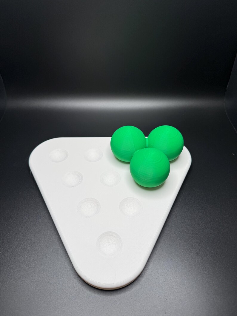 May include: A white triangular tray with seven circular indentations, three green balls are sitting on top of the tray.