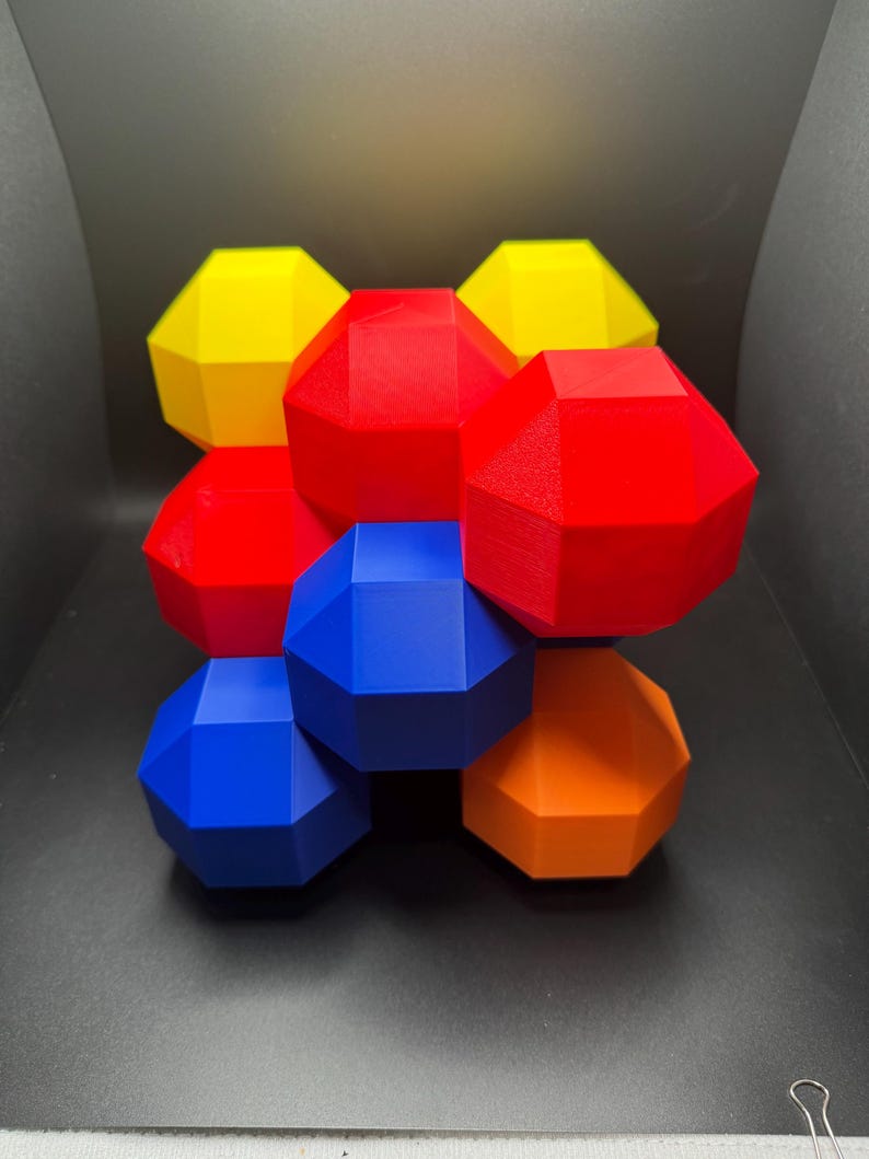 May include: A geometric sculpture made of 8 connected, multi-faceted shapes. The shapes are in red, yellow, blue, and orange.