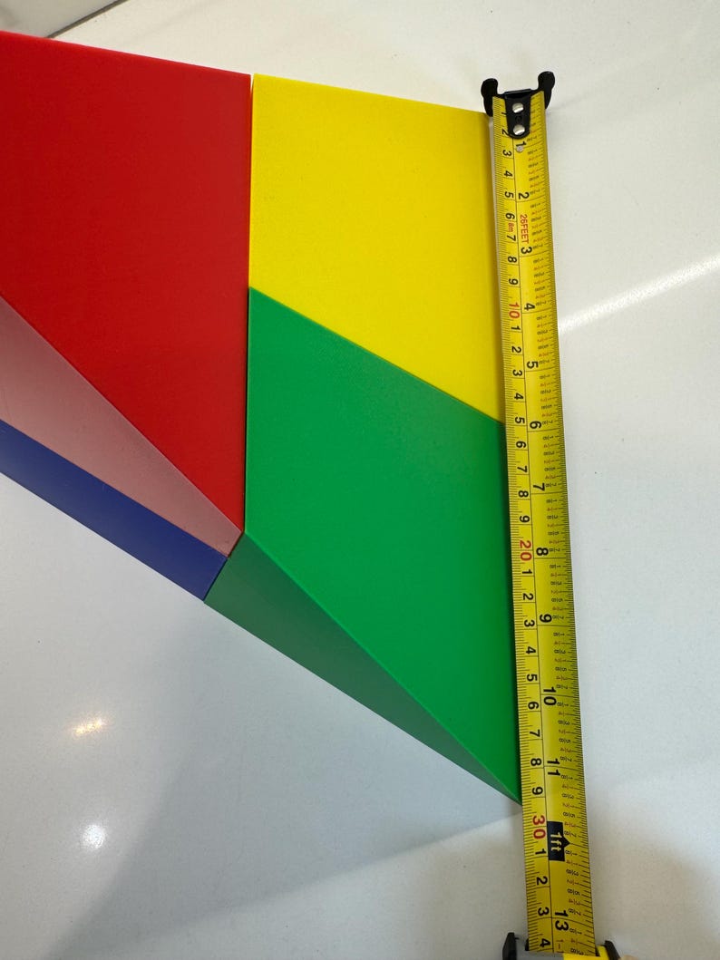 May include: A colorful geometric shape made of four pieces of cardboard. The pieces are red, yellow, green, and blue. The shape is measured with a tape measure, which shows a measurement of 11 inches.