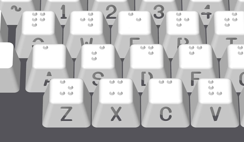 May include: A white keyboard with braille markings on the keys. The keys are labeled with letters and numbers. The keyboard is on a gray surface.