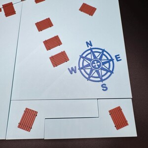 May include: A light blue game board with a blue compass rose and several small, reddish-brown rectangular pieces scattered across the surface. The compass rose indicates North, South, East, and West.