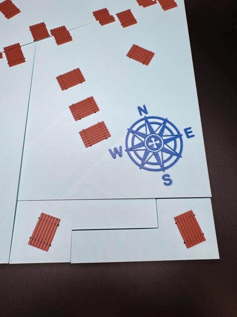 May include: A light blue game board with a blue compass rose and several small, reddish-brown rectangular pieces scattered across the surface. The compass rose indicates North, South, East, and West.
