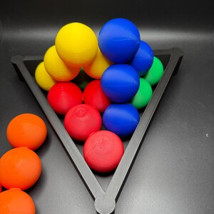 Peut inclure: Un r&acirc;telier triangulaire noir contient une pyramide de boules color&eacute;es. Les boules sont rouges, jaunes, bleues et vertes. Il y a quatre boules orange en dehors du r&acirc;telier.