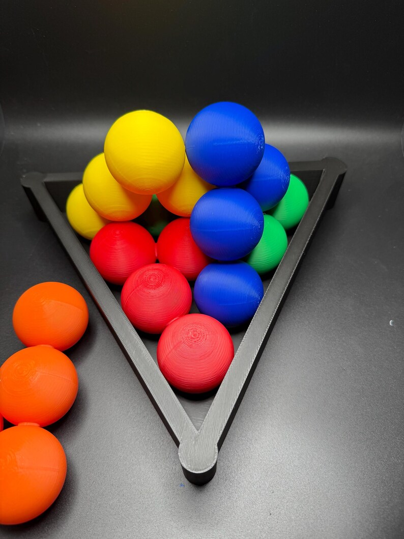 Peut inclure: Un r&acirc;telier triangulaire noir contient une pyramide de boules color&eacute;es. Les boules sont rouges, jaunes, bleues et vertes. Il y a quatre boules orange en dehors du r&acirc;telier.