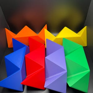 May include: A set of six colorful geometric shapes, each with a unique design. The shapes are arranged in a rainbow pattern, starting with orange and ending with green. The shapes are made of a smooth, glossy material.