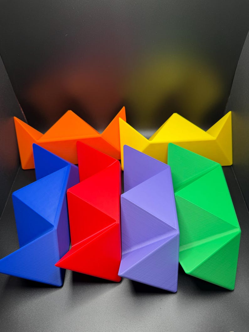 May include: A set of six colorful geometric shapes, each with a unique design. The shapes are arranged in a rainbow pattern, starting with orange and ending with green. The shapes are made of a smooth, glossy material.