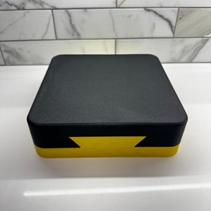 May include: A black and yellow rectangular box with a textured lid. The box is closed.