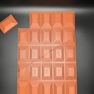 Op de afbeelding: Een grote, oranje-bruine chocolade reep met een textuur. De reep is gebroken in 24 vierkanten.