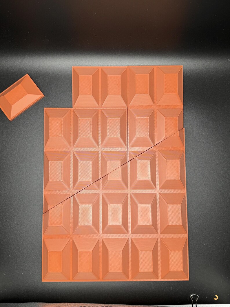 Op de afbeelding: Een grote, oranje-bruine chocolade reep met een textuur. De reep is gebroken in 24 vierkanten.