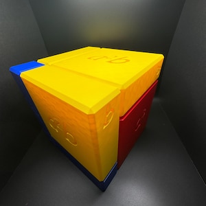 May include: A yellow, red, and blue cube puzzle with the letters "C.R.I.B." printed on the sides.