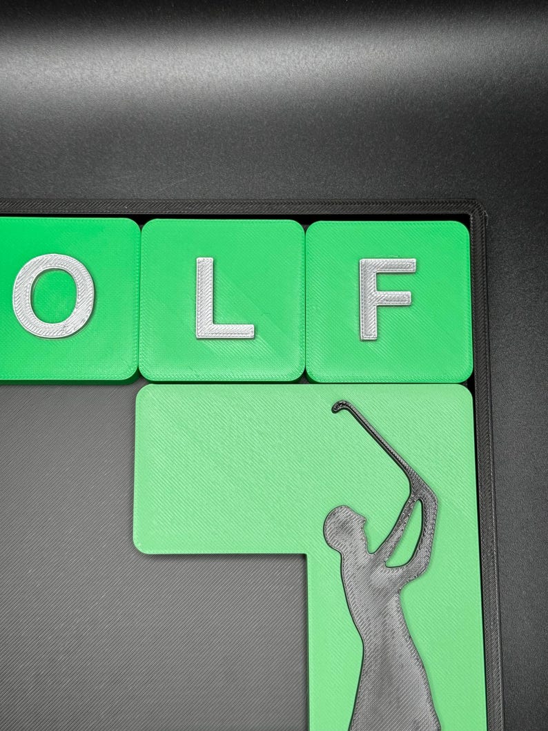 May include: Green and white tile letters spelling "GOLF" with a green background and a black silhouette of a golfer swinging a club.