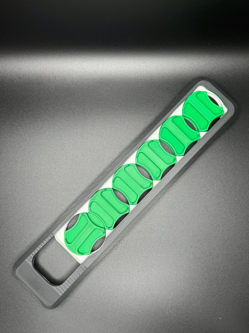May include: A black and white plastic tool with a handle and eight green circular slots. The tool is designed to hold and organize small round objects.