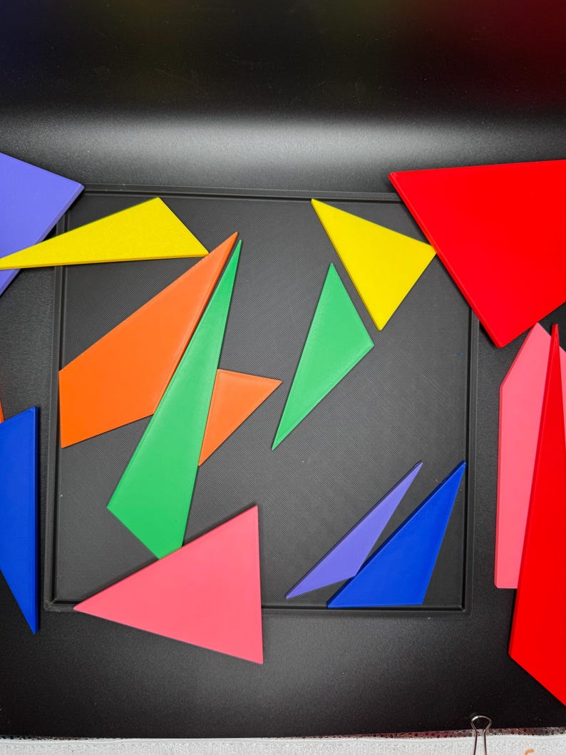May include: A set of colorful geometric shapes, including triangles in red, orange, yellow, green, blue, and pink, arranged on a black surface.