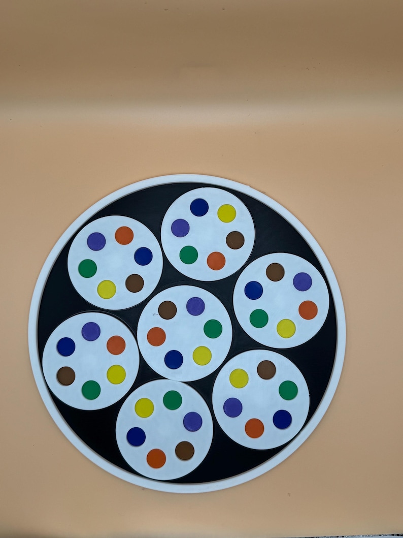May include: A circular game board with a black center and white border. Seven white circles are arranged within the black center, each with six colored dots: orange, blue, green, yellow, purple, and brown. The background is a solid peach color.