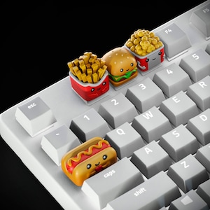 May include: A white keyboard with keycaps shaped like various fast food items, including a hamburger, french fries, a hot dog, and popcorn. The keycaps all have smiling faces and look cute.