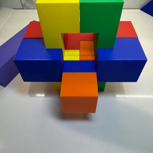 May include: A colorful wooden puzzle with six blocks in red, blue, yellow, green, and orange. The blocks are arranged in a complex pattern, creating a three-dimensional shape.