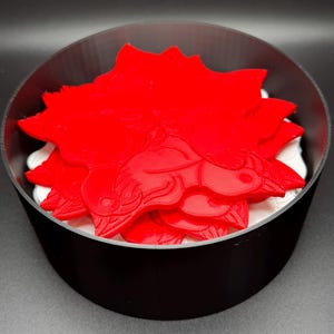 May include: A stack of red 3D printed dragon-shaped coasters in a black circular container.