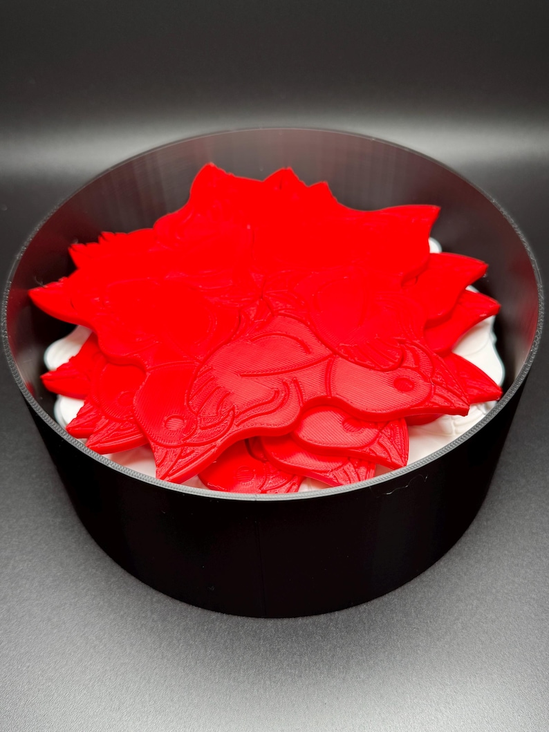 May include: A stack of red 3D printed dragon-shaped coasters in a black circular container.