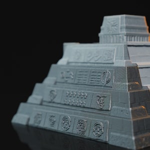 May include: A gray 3D printed model of a Mayan pyramid with intricate details and carvings. The pyramid has multiple levels and a flat top with a small structure on it.