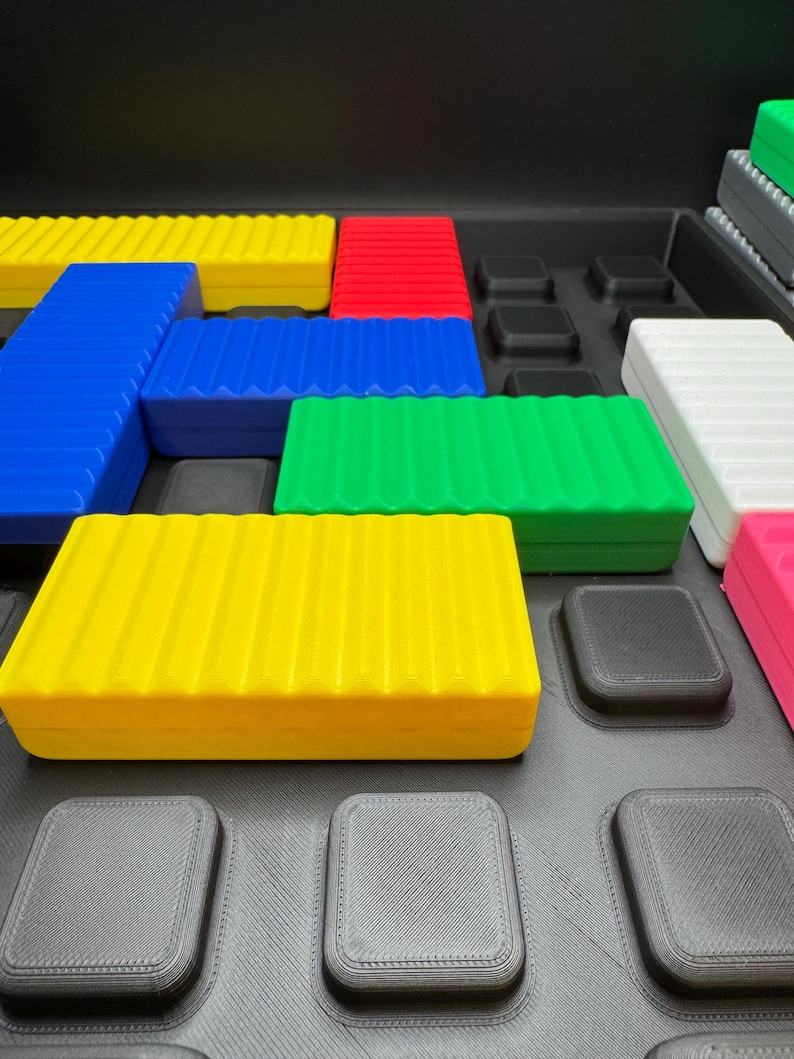 May include: A collection of colorful, rectangular, ridged blocks in yellow, blue, green, red, white, and pink. The blocks are arranged on a black surface with square indentations. The blocks appear to be part of a puzzle or building set.