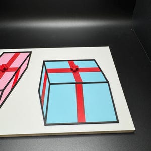 May include: A light blue gift box with a red ribbon and bow, and a pink gift box with a red ribbon and bow. Both boxes have black outlines and are on a white surface.