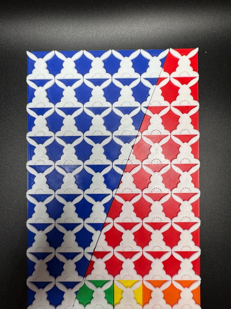 May include: A close-up of a 3D printed tile pattern with white bunny silhouettes on a blue background on the left side of the image and a red background on the right side of the image. The bottom of the image shows a row of tiles in green, yellow, and orange.