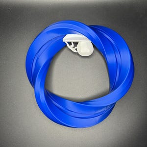Może przedstawiać: Niebieski plastikowy pierścień o skręconym wzorze. Pierścień wykonany jest z jednego kawałka plastiku i ma średnicę około 25 cm.